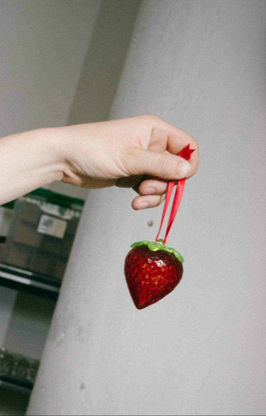 Person holding a decorative strawberry with a red ribbon against a neutral background